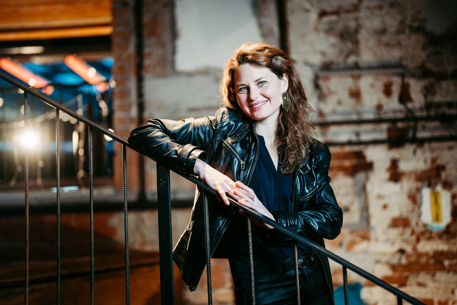 A woman in a black leather jacket leaning on a railing